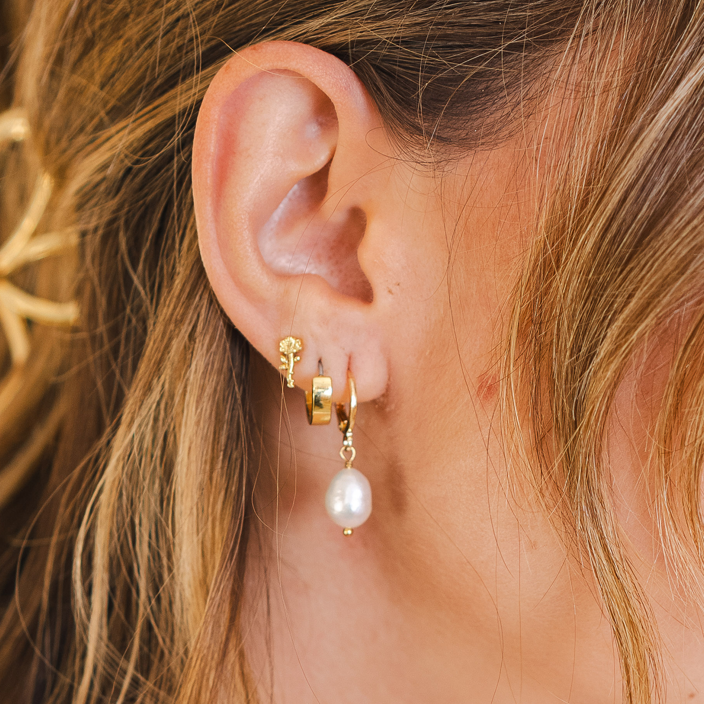 Close-up of an ear wearing gold hoop earrings with a pearl drop earring.