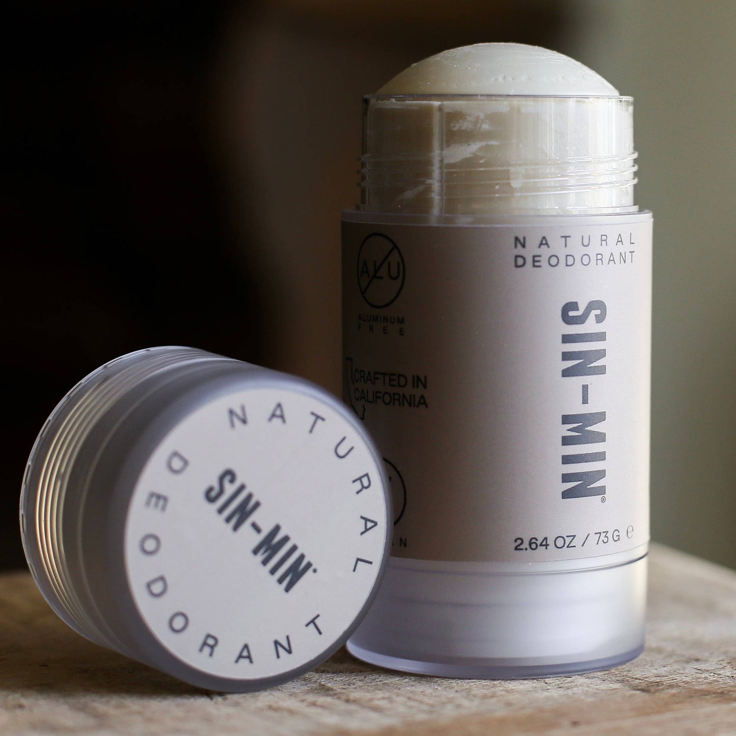 Two SIN-MIN natural deodorants on a wooden surface with a blurred background