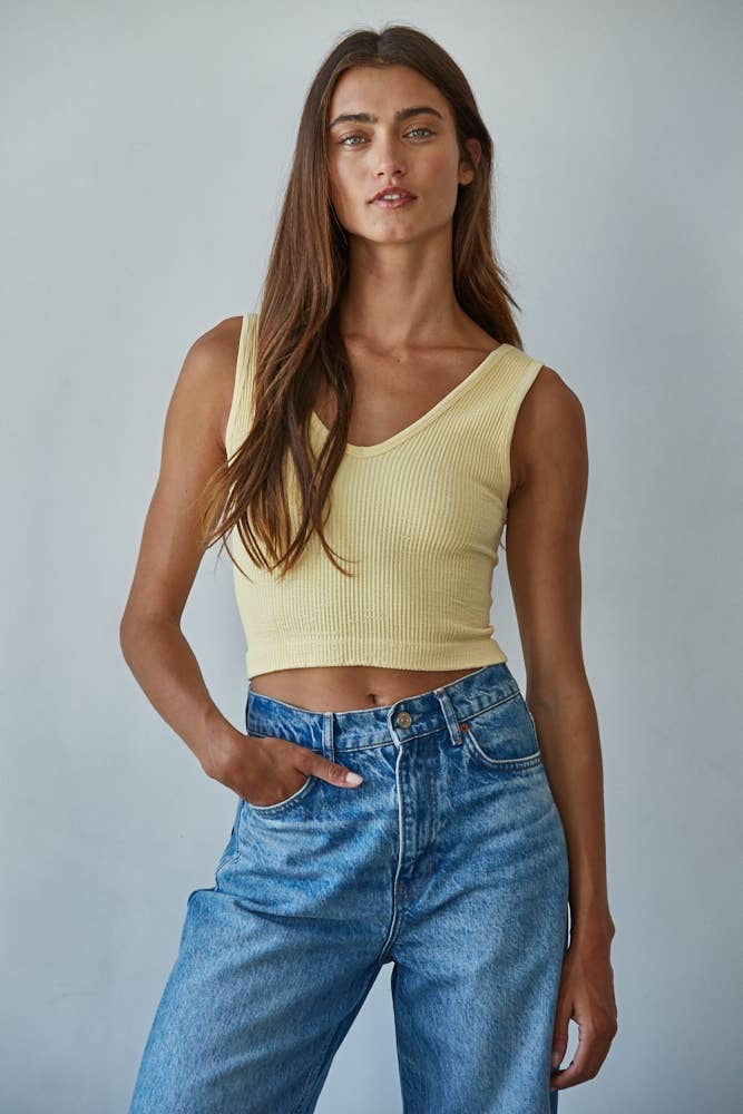 Woman wearing a yellow tank top and blue jeans against a plain background