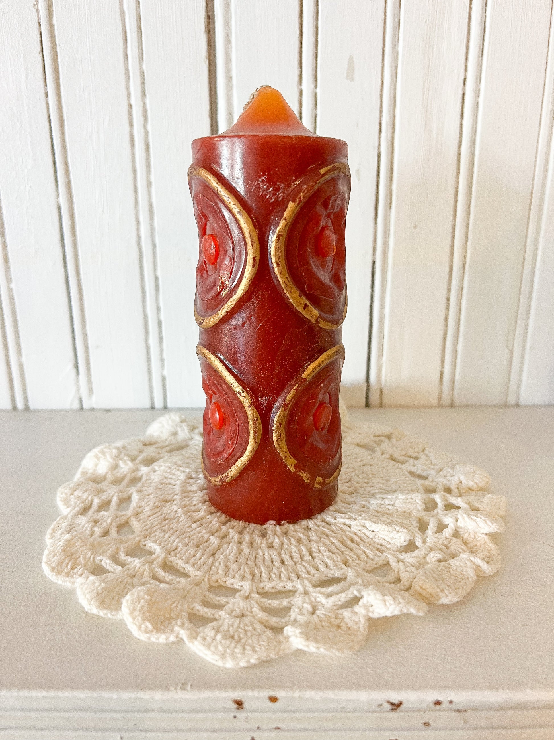 vintage red pillar candle with gold embossed scroll pattern sitting on a white crocheted doily