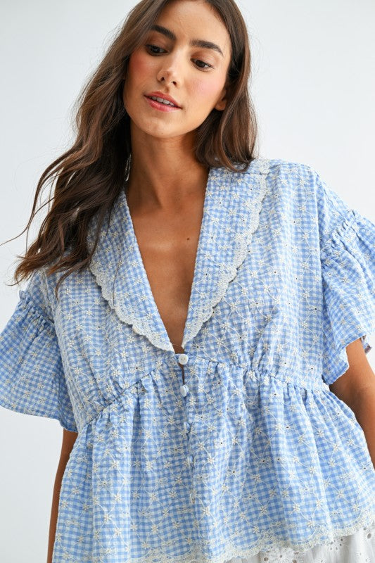 Blue gingham blouse featuring a scalloped collar, flutter sleeves, and a relaxed feminine fit.