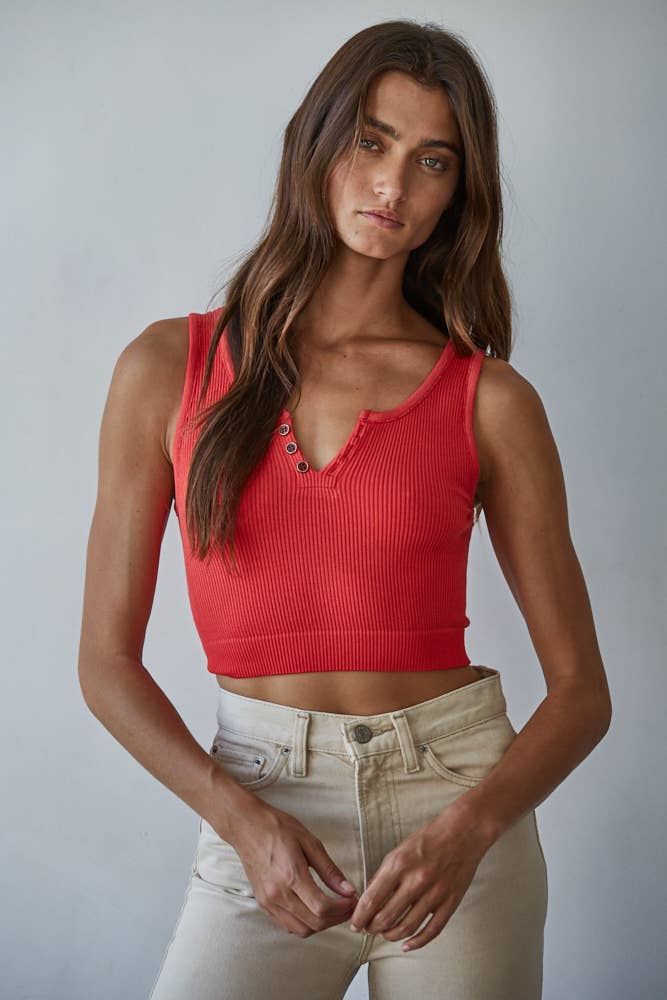 Woman wearing a red sleeveless top and light-colored pants against a plain background