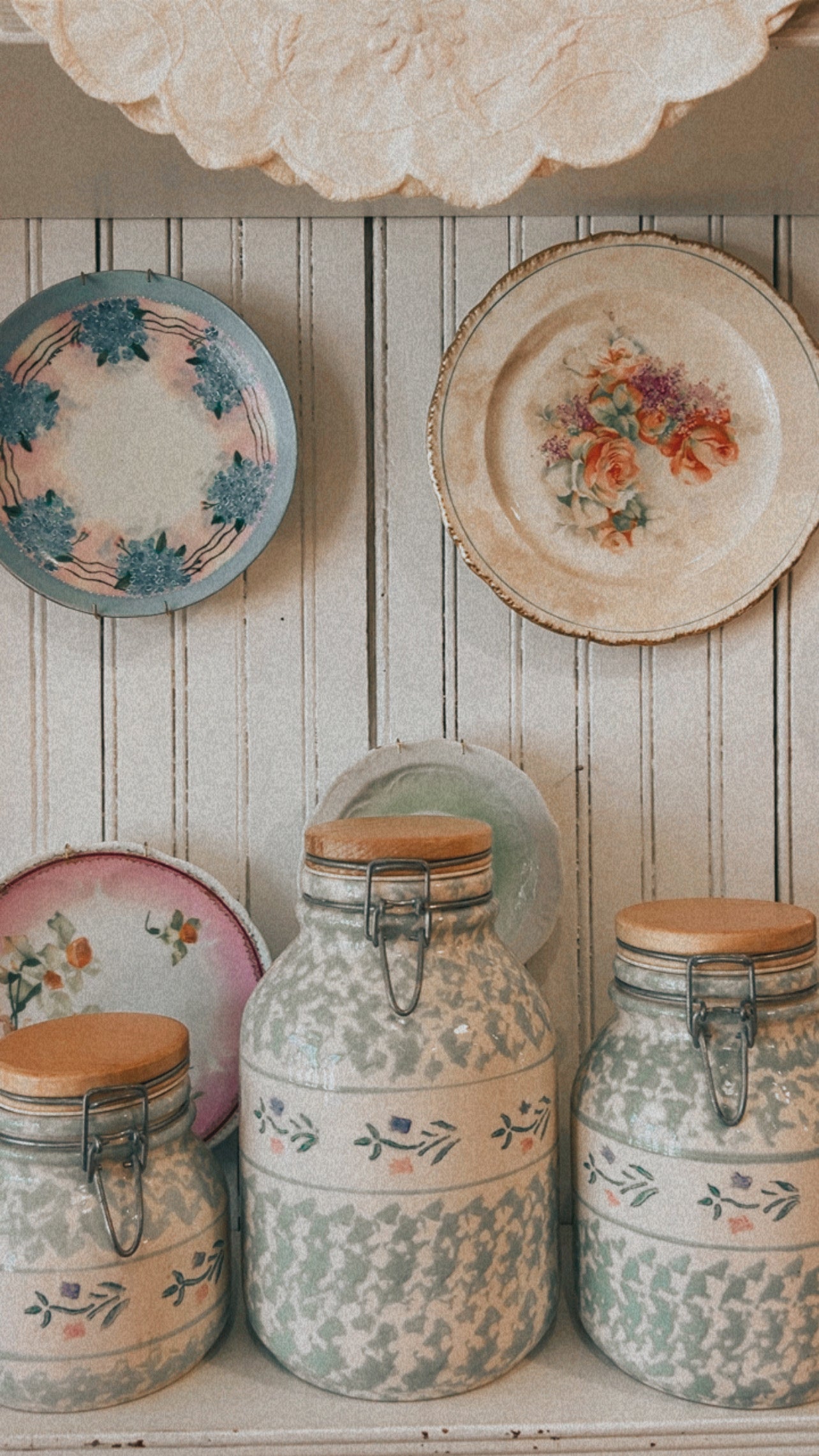 Decorative plates and jars with floral patterns on a wooden shelf.