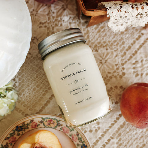 Georgia Peach 16 oz soy candle by Antique Candle Co styled on lace table with fresh sliced peaches and farmhouse decor.
