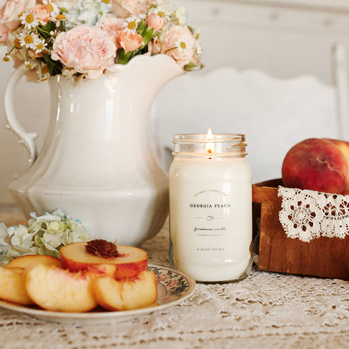 Lit Georgia Peach soy candle 16 oz in mason jar with fresh peaches and floral farmhouse kitchen decor.
