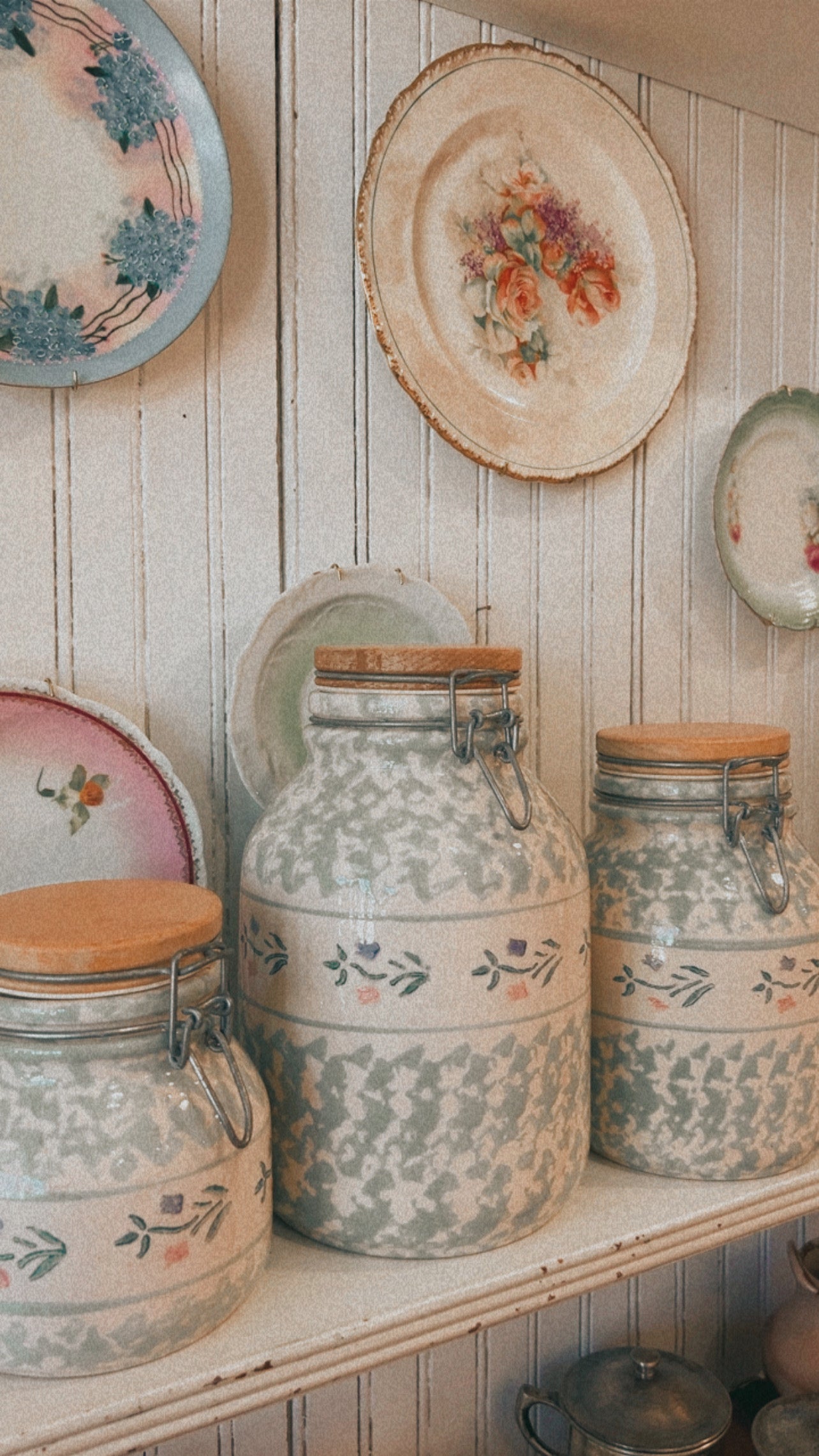 Decorative ceramic jars with floral patterns on a wooden shelf against a wooden wall.