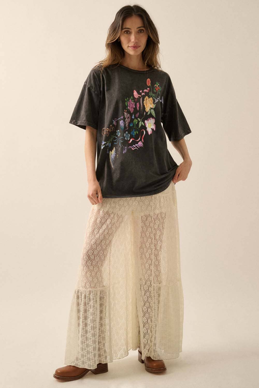 Woman wearing a black t-shirt with colorful floral design and beige lace pants on a plain background