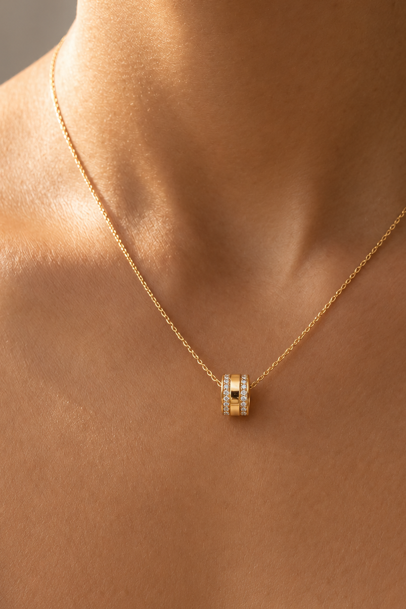     Model wearing a delicate gold-tone necklace with a sparkling barrel pendant.