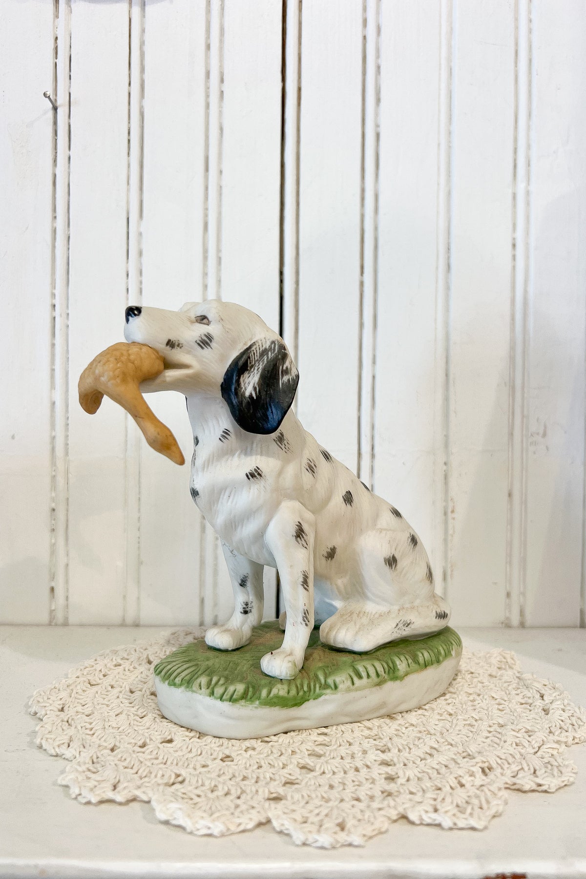 Vintage 6-inch porcelain black and white hunting dog figurine holding a game bird with a green grass base.