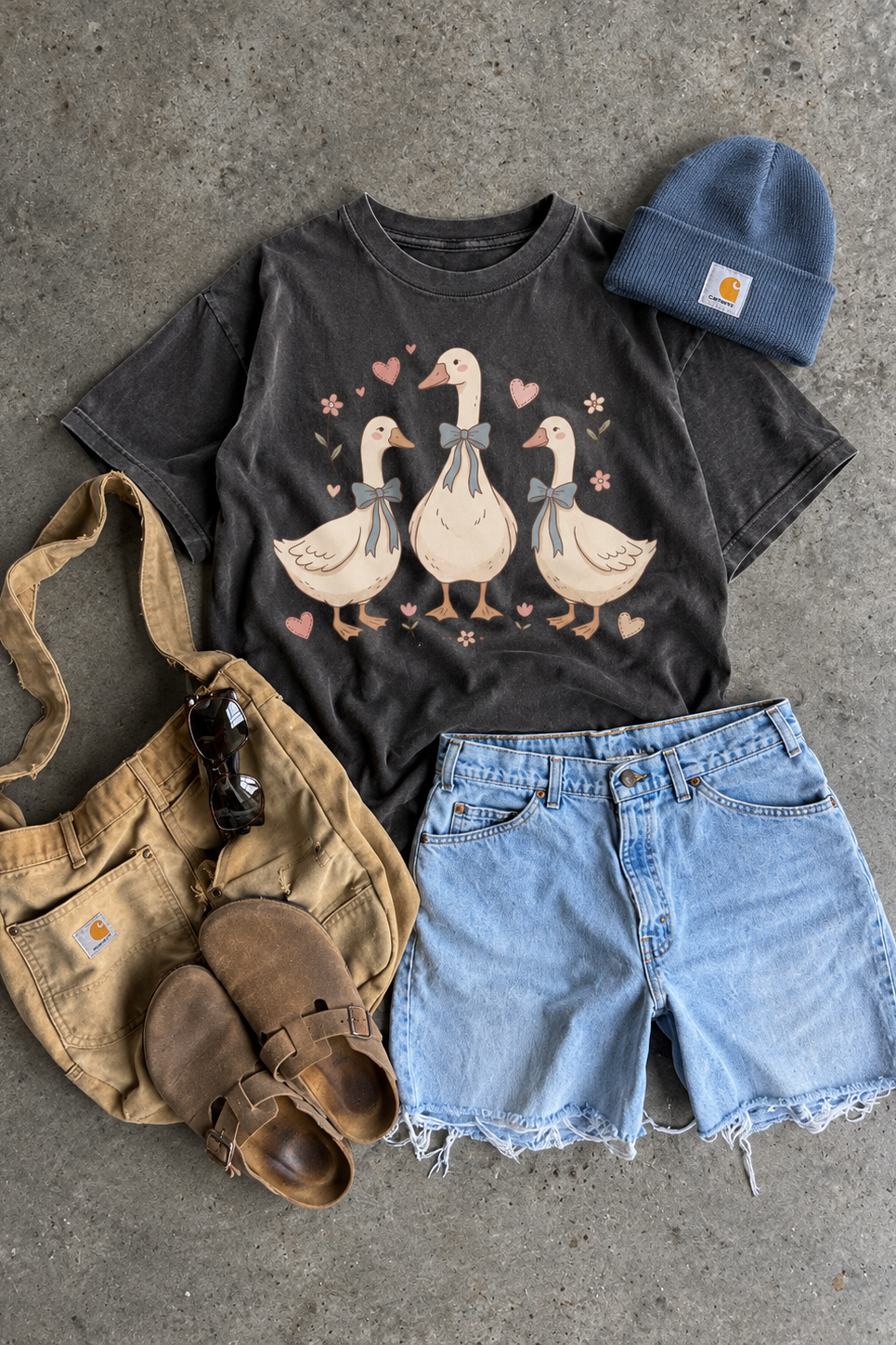 Pepper Comfort Colors graphic tee featuring three geese with blue bows, pink hearts, and small flowers, styled with denim shorts and a blue beanie.