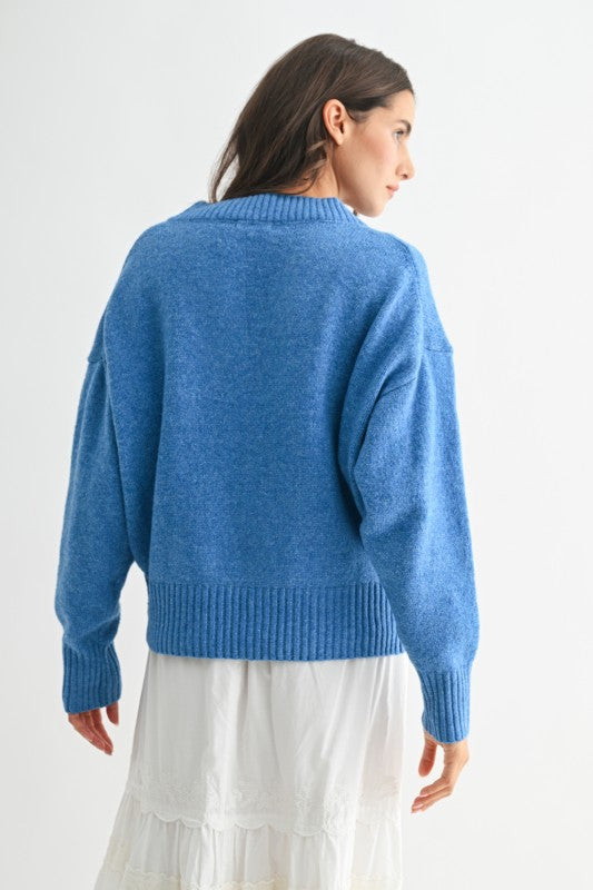Back view of the cornflower blue knit sweater showing ribbed hem and cuffs, paired with a white ruffled skirt.