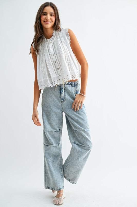 Woman wearing a white sleeveless top with lace details and light blue jeans on a white background