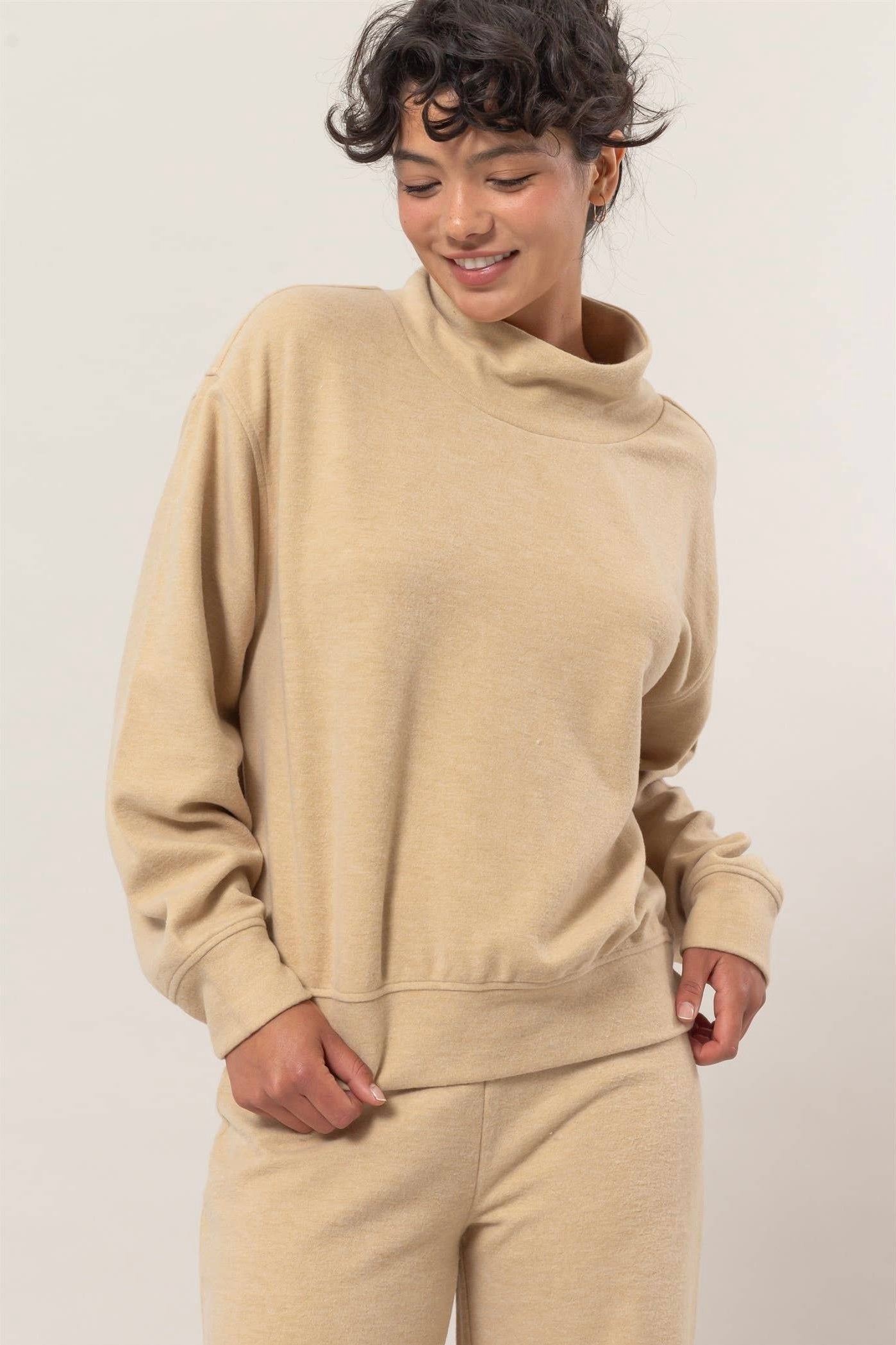Neutral oatmeal lounge pullover with a rolled mock neck and relaxed fit, styled on model with matching soft knit pants. Minimal, cozy, and perfect for everyday wear.