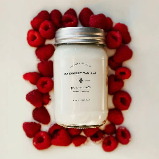 Raspberry Vanilla 16 oz soy candle surrounded by fresh raspberries showcasing fruity vanilla spring scent.