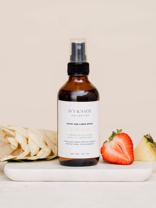 Brown spray bottle labeled 'Ivy & Sage' on a white surface with strawberries and flowers.