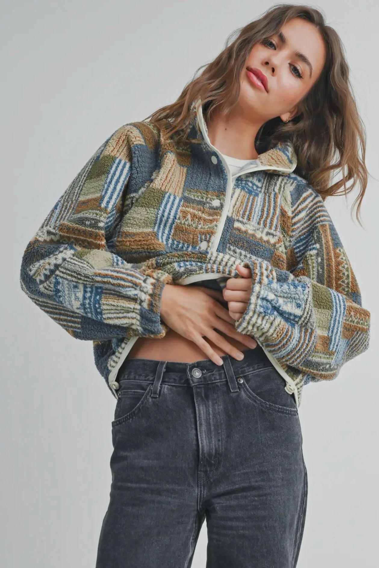 Side view of a woman wearing a soft sherpa pullover with a colorful patchwork pattern. The half-zip neckline and front pocket give it a casual, cozy mountain-lodge look.