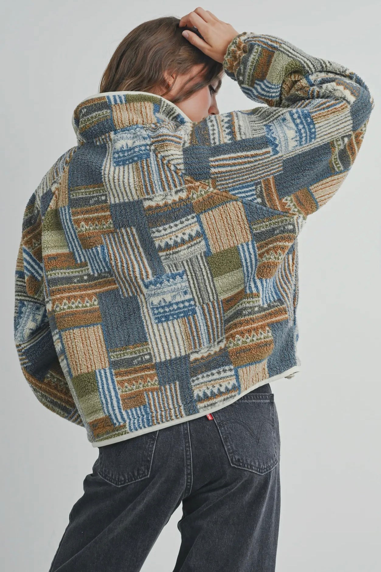 Back view of a sherpa fleece pullover featuring rustic patchwork squares in earthy blue, green, and rust hues. The jacket has a slouchy, relaxed silhouette.