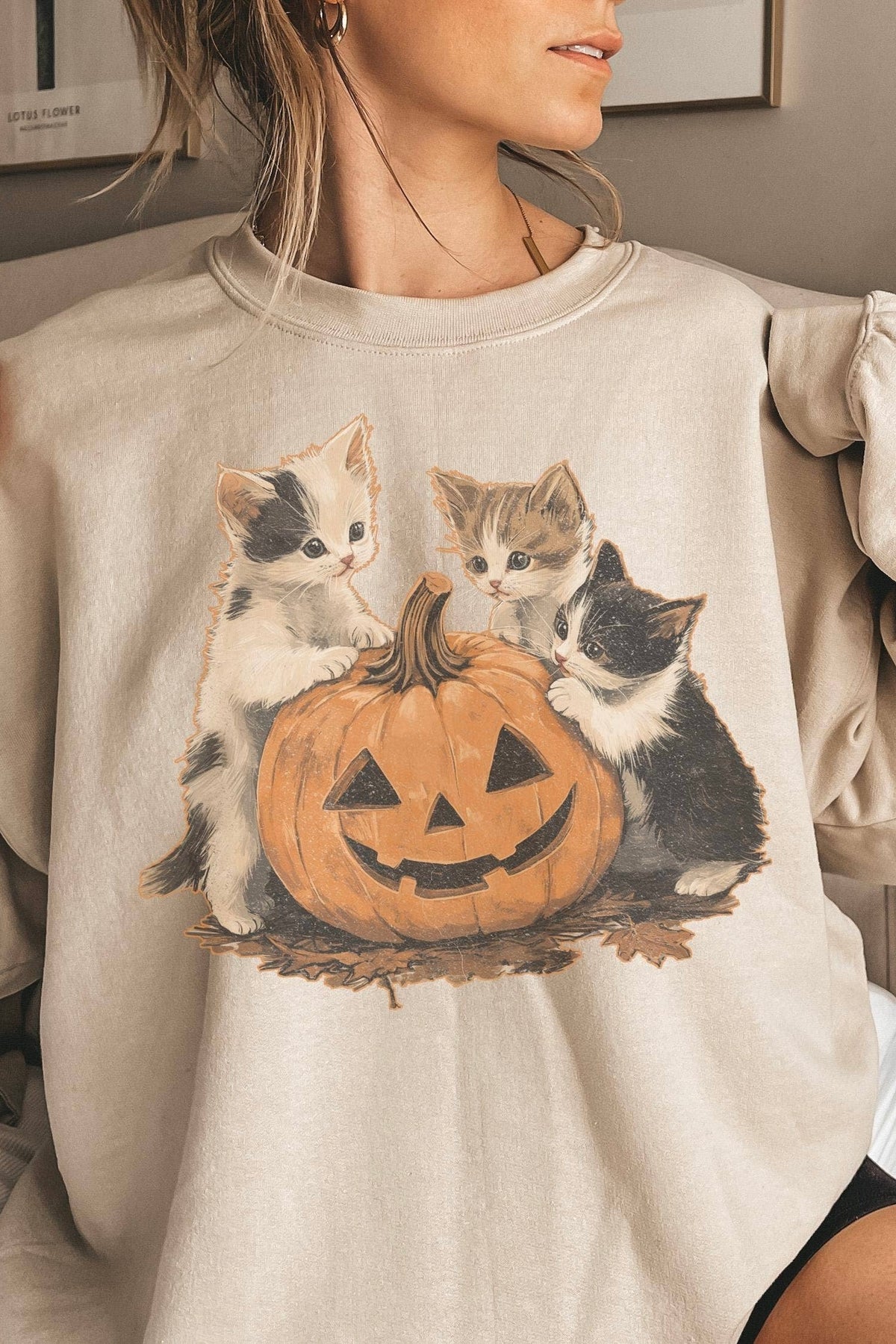 Woman wearing a vintage cream Halloween sweatshirt with three kittens gathered around a smiling jack-o’-lantern.