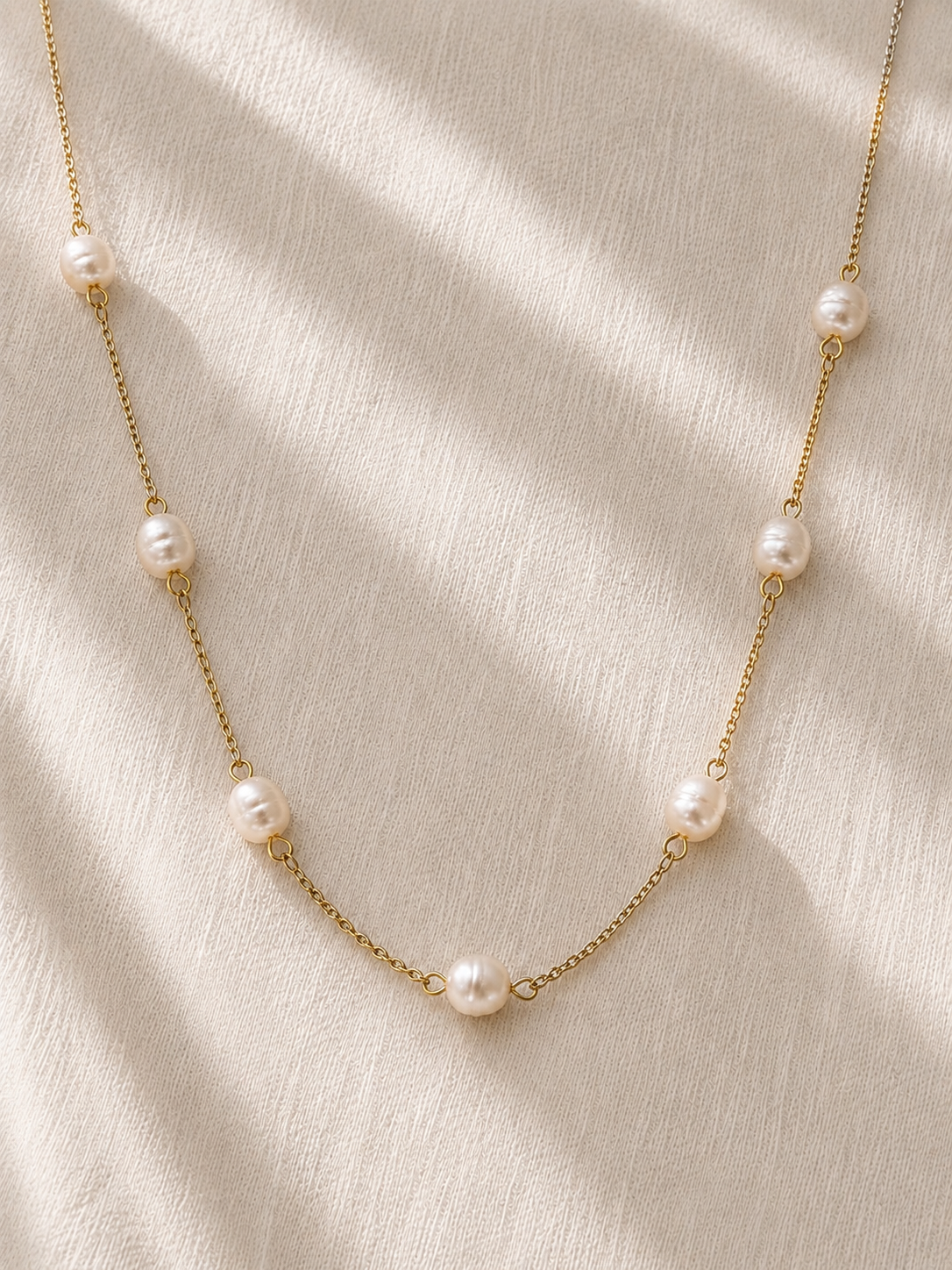 Delicate gold station necklace featuring naturally irregular freshwater pearls displayed on soft ivory linen.
