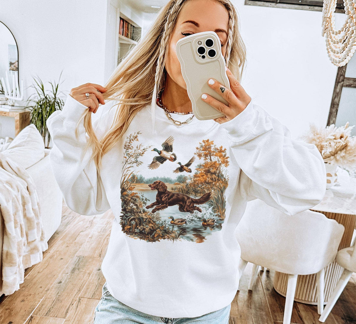 Woman wearing the ash-gray Mallard Run Sweatshirt featuring a vintage hunting dog, mallards, autumn trees, and marsh artwork.