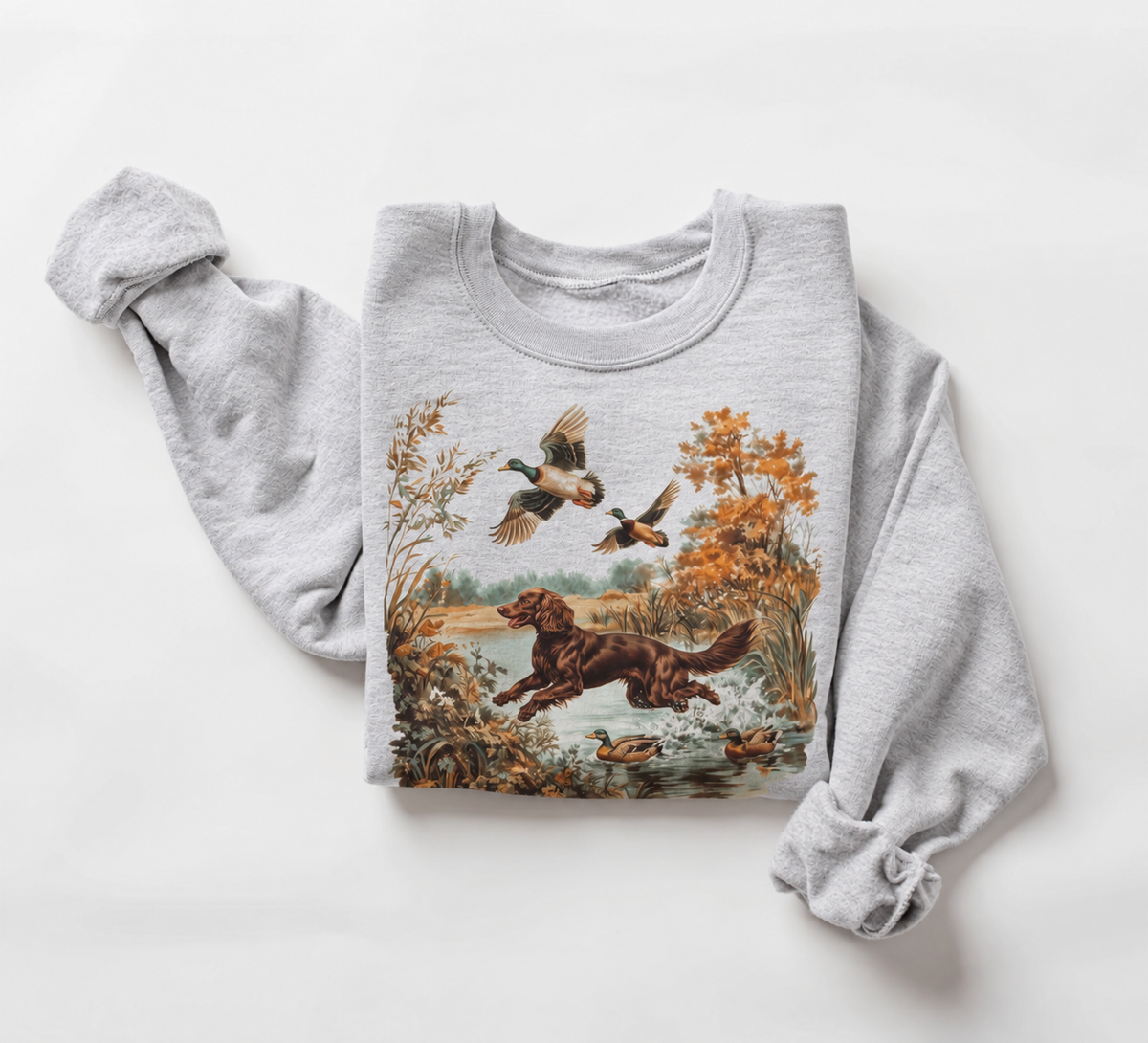 Folded ash-gray Mallard Run Sweatshirt featuring vintage artwork of a hunting dog running through an autumn marsh with flying mallards.