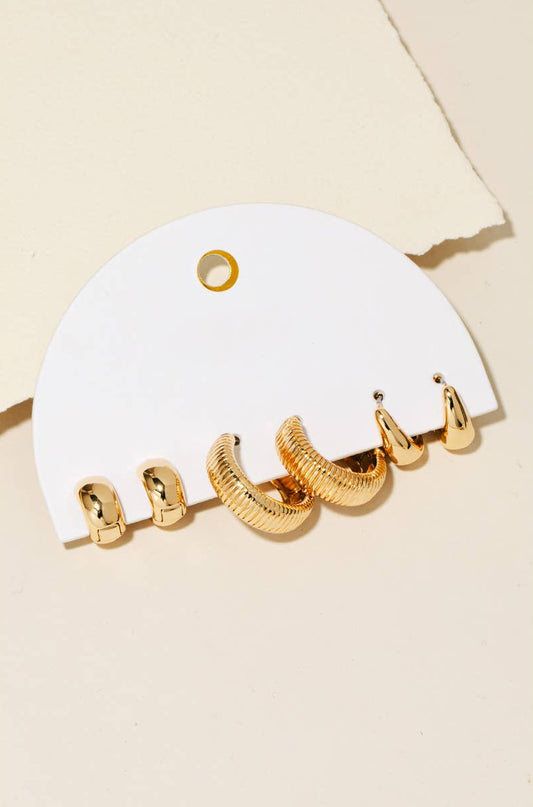A three-pair gold hoop earring set displayed on a white card against a soft neutral background, featuring ribbed, smooth, and tapered mini hoops — modern, minimal boutique jewelry.
