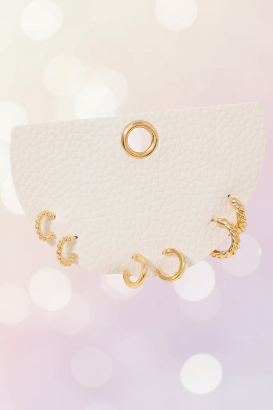 Three-pair dainty gold mini hoop earring set on a white card against a soft dreamy background, featuring beaded, smooth, and twisted textures — minimal, feminine boutique jewelry.
