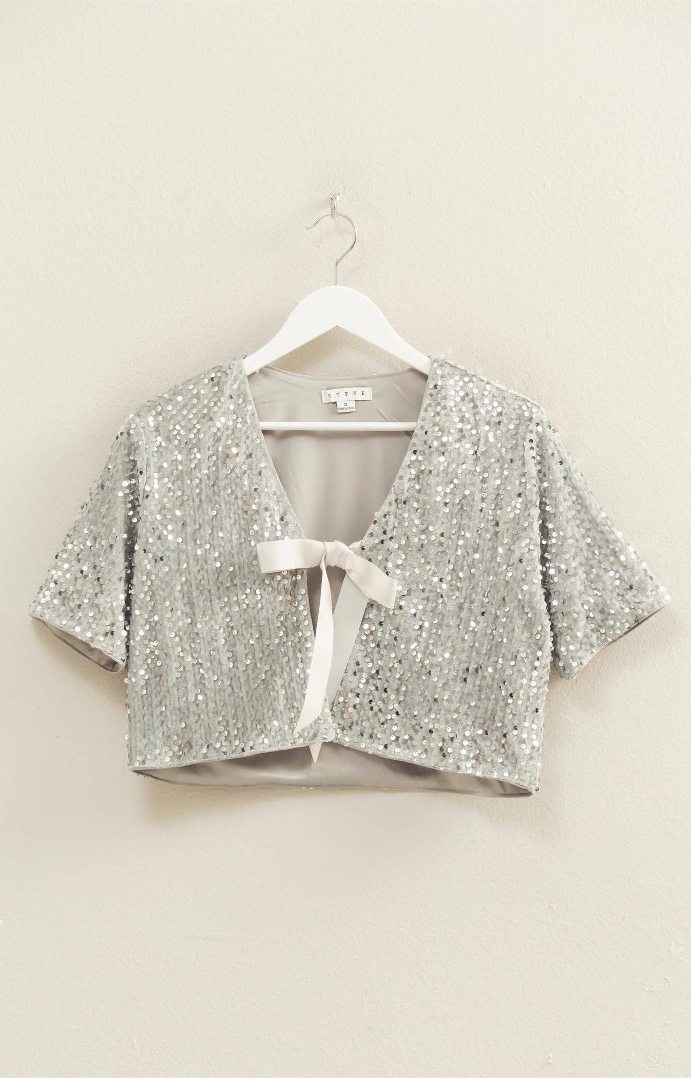 Silver sequin tie-front cropped top layered over white tank on model.