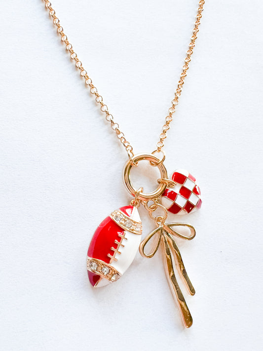 Gold chain necklace with red and white football charm, red-and-white checker heart charm, and gold bow on a clean white background.