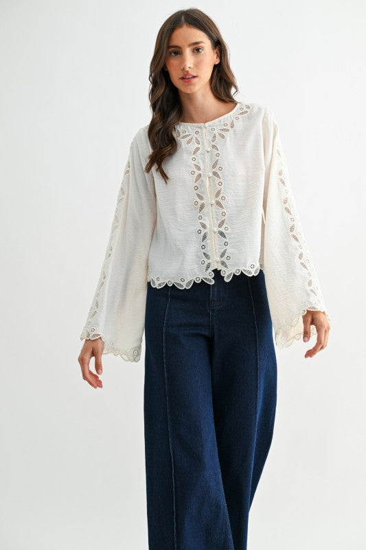 Ivory vintage-inspired lace blouse with long sleeves and scalloped hem worn with dark denim pants