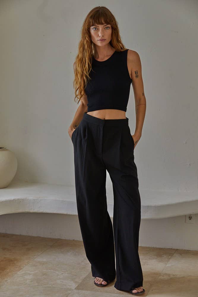 Woman wearing a black sleeveless top and wide-leg pants against a neutral background