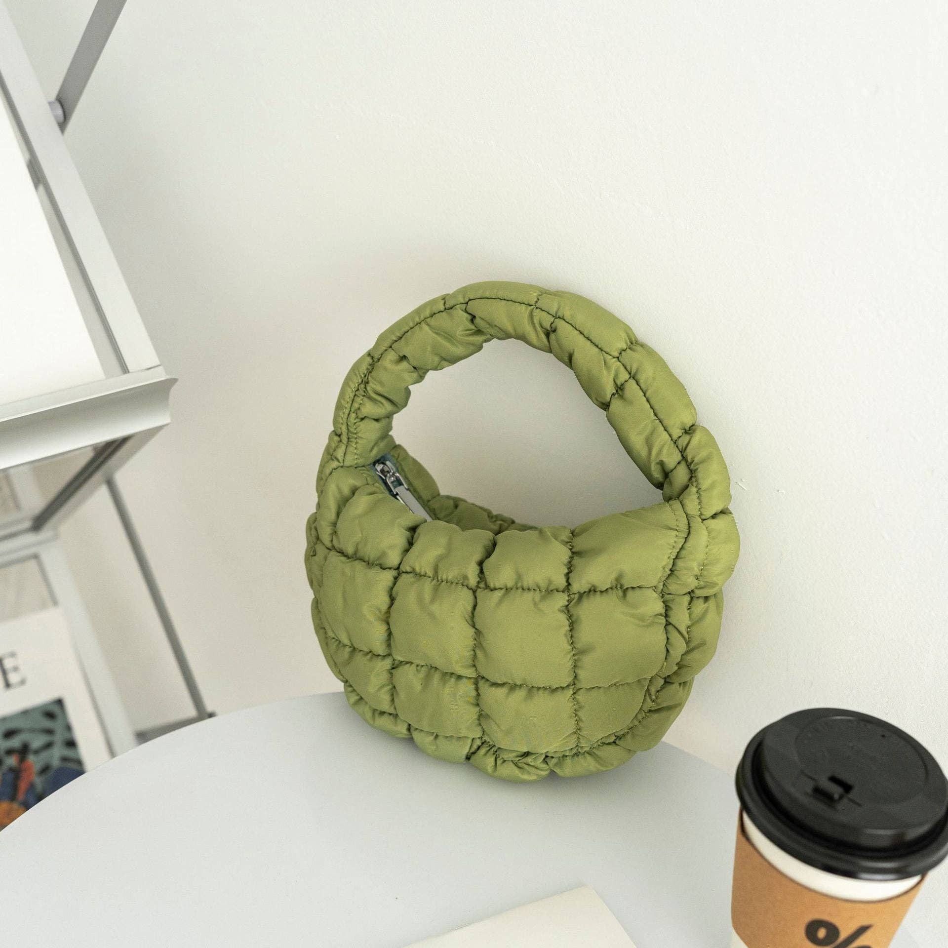 Green quilted handbag on a white surface with a coffee cup in the background