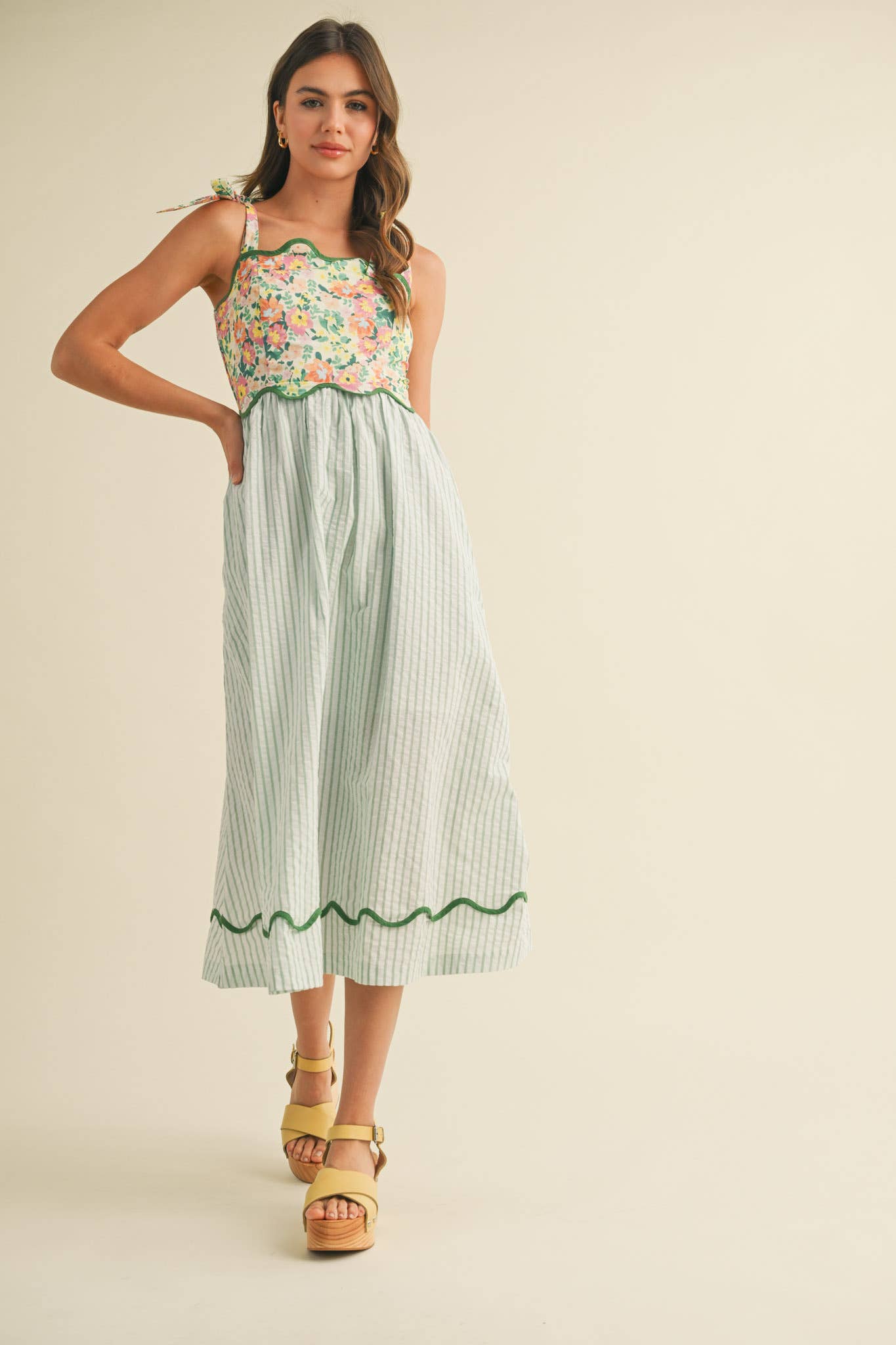 Woman wearing a floral top and striped skirt with yellow sandals on a beige background