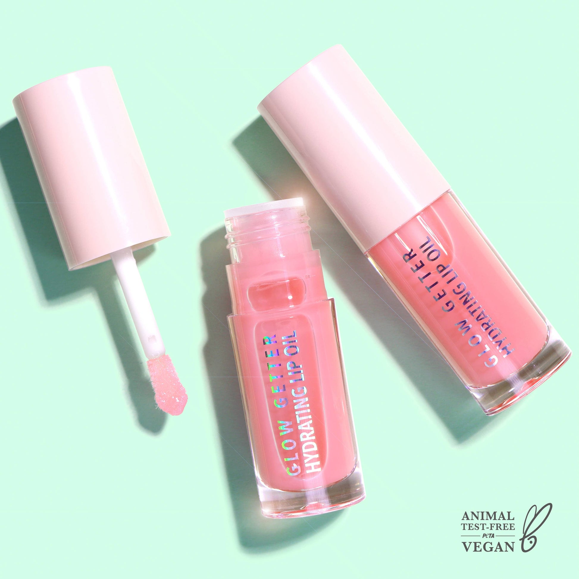 Pink lip gloss with applicator on a light green background