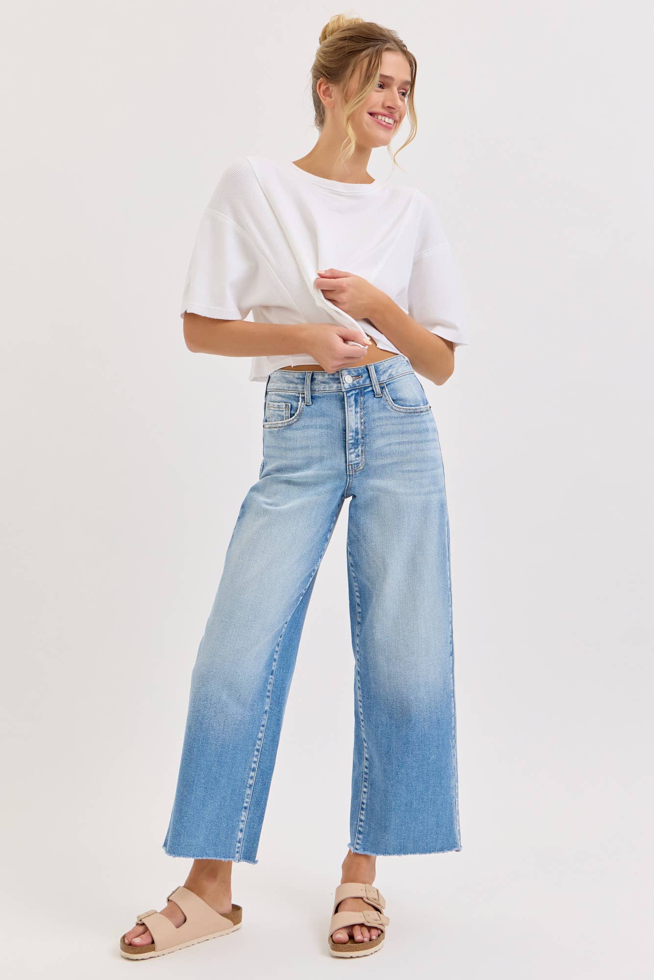 Woman wearing light blue jeans and a white top on a plain background