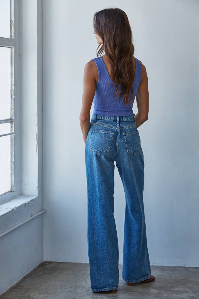Woman wearing a blue tank top and jeans standing in a room with a window.