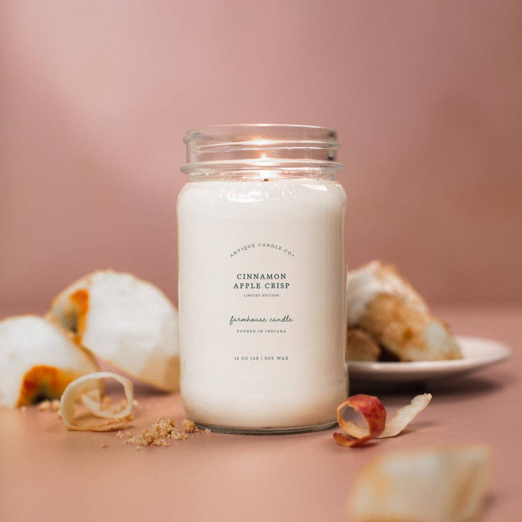 Candle labeled 'Cinnamon Apple Crisp' with autumn-themed elements on a pink background