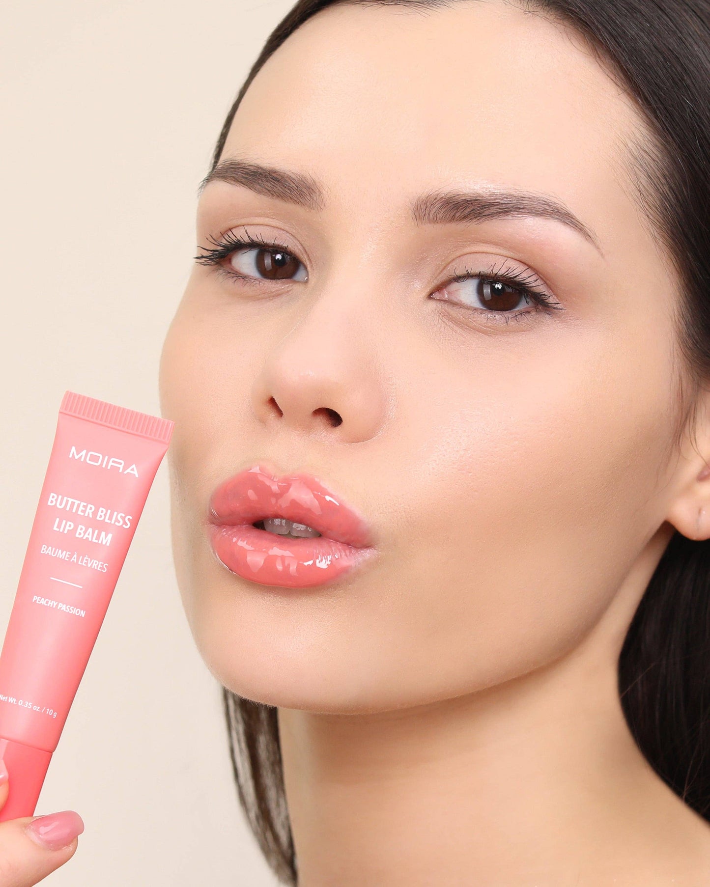 Woman holding a pink lip balm tube with a beige background