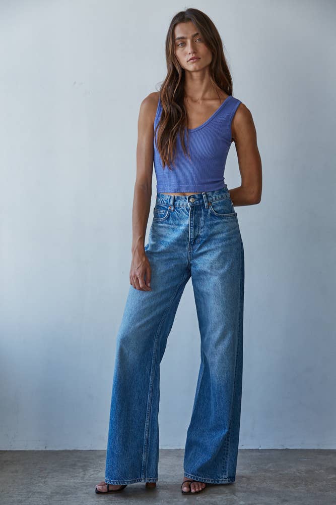 Woman wearing a blue sleeveless top and wide-leg jeans against a plain background