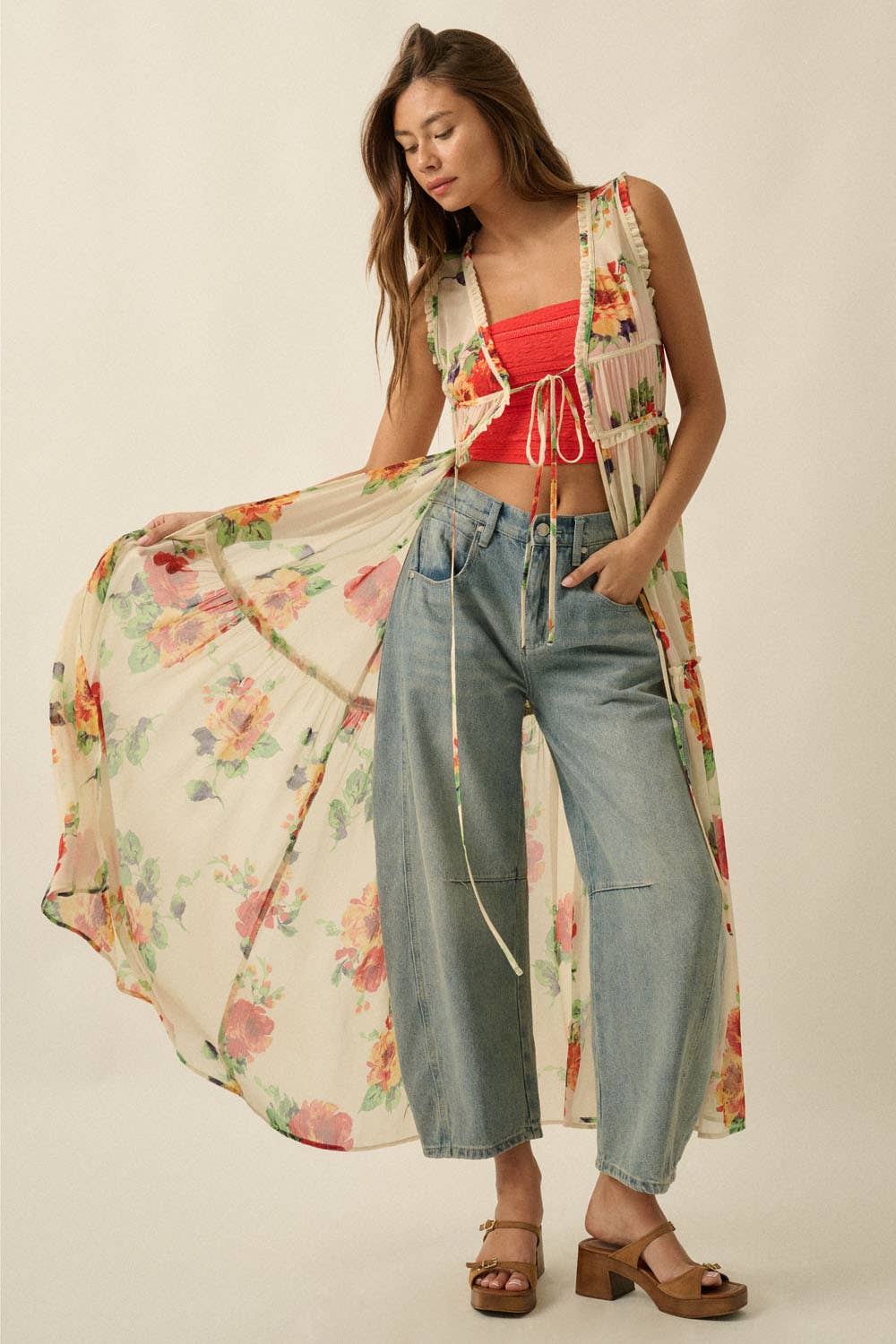 Woman wearing a floral cover-up, red top, and blue jeans on a plain background