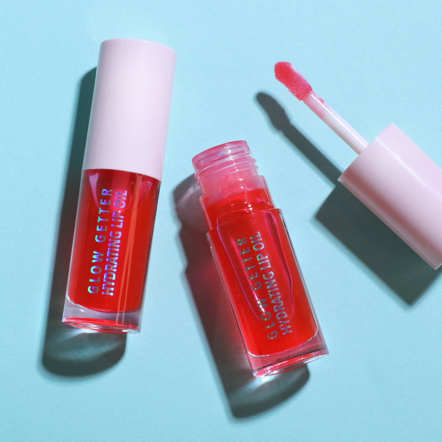 Red lip gloss with applicator on a light blue background