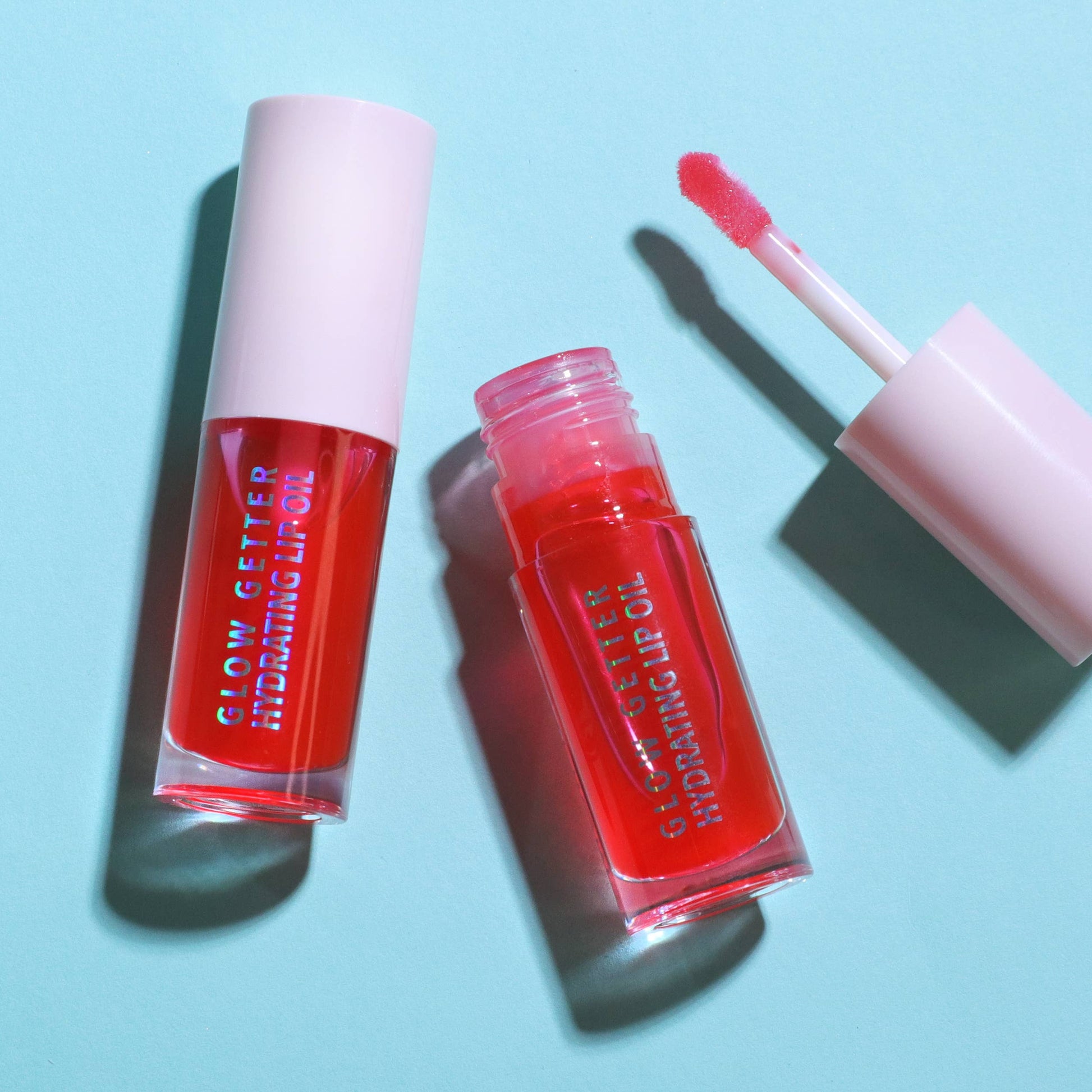 Red lip gloss with applicator on a light blue background