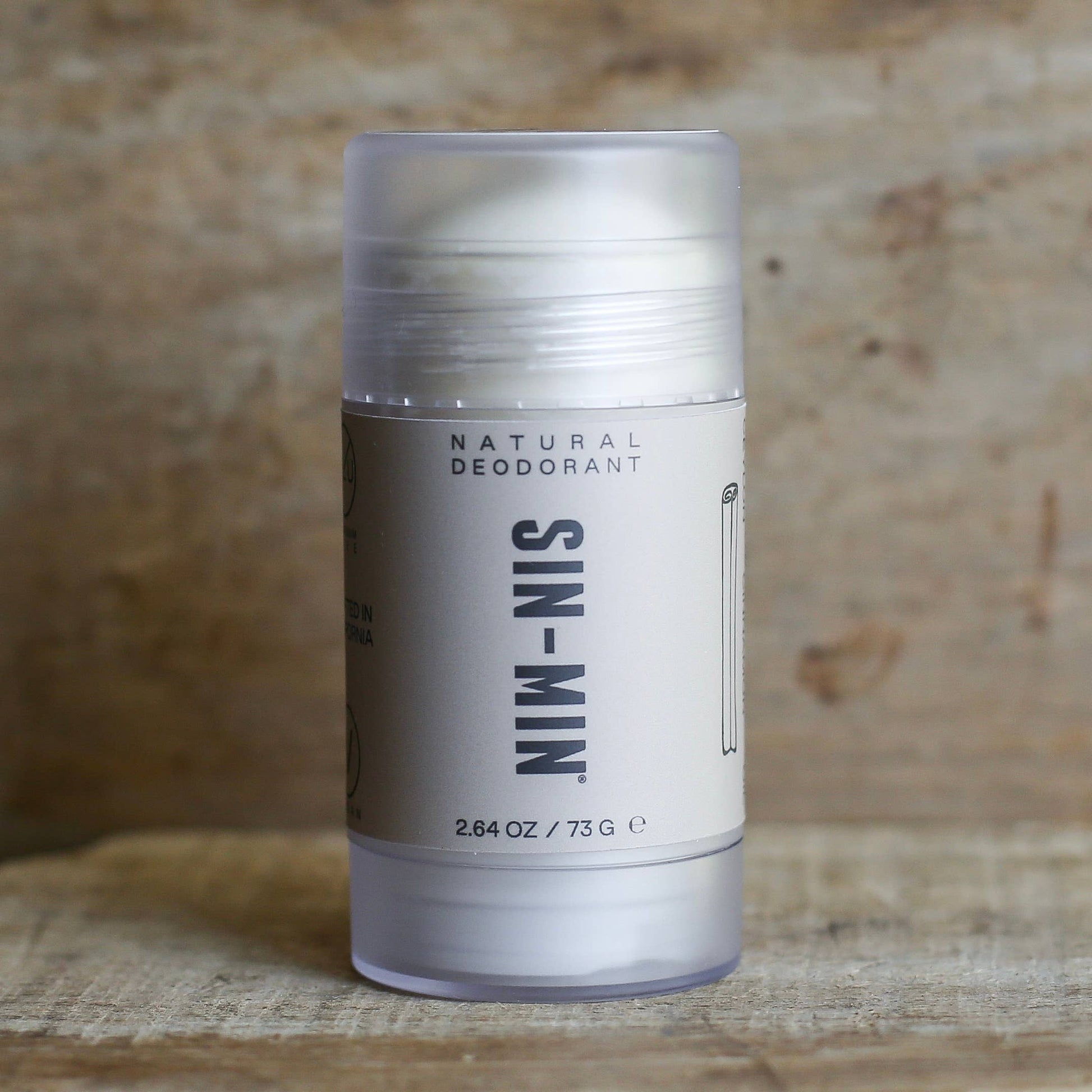 Natural deodorant stick with 'SIN-MIN' branding on a wooden background