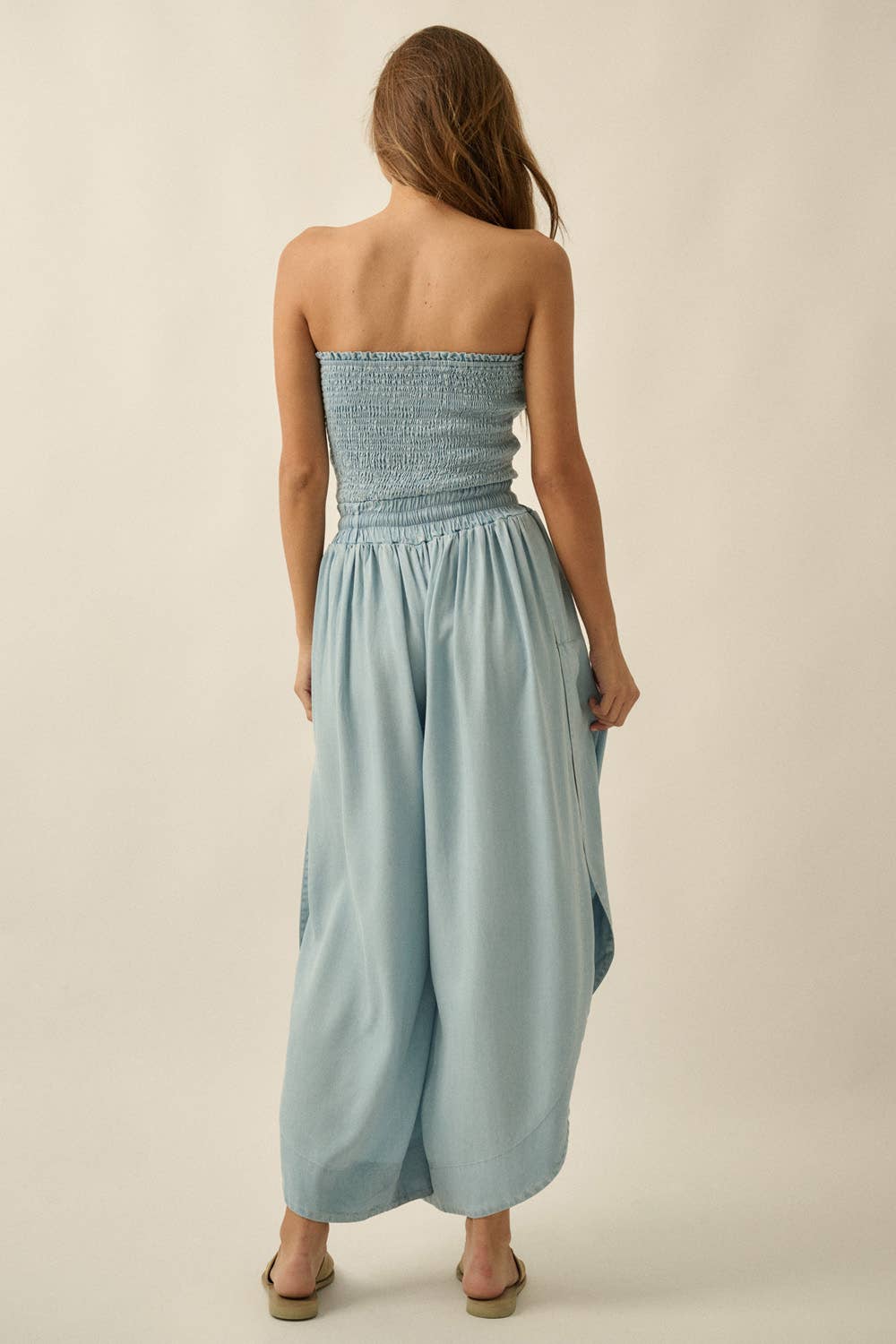 Woman wearing a light blue strapless jumpsuit on a beige background