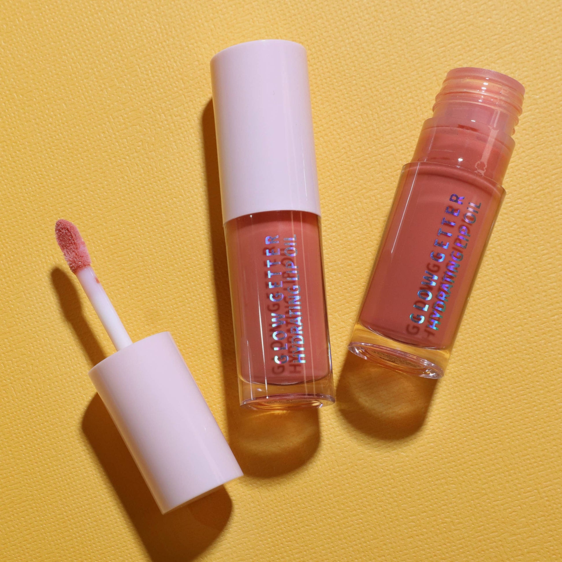 Two lip gloss products with applicators on a yellow background