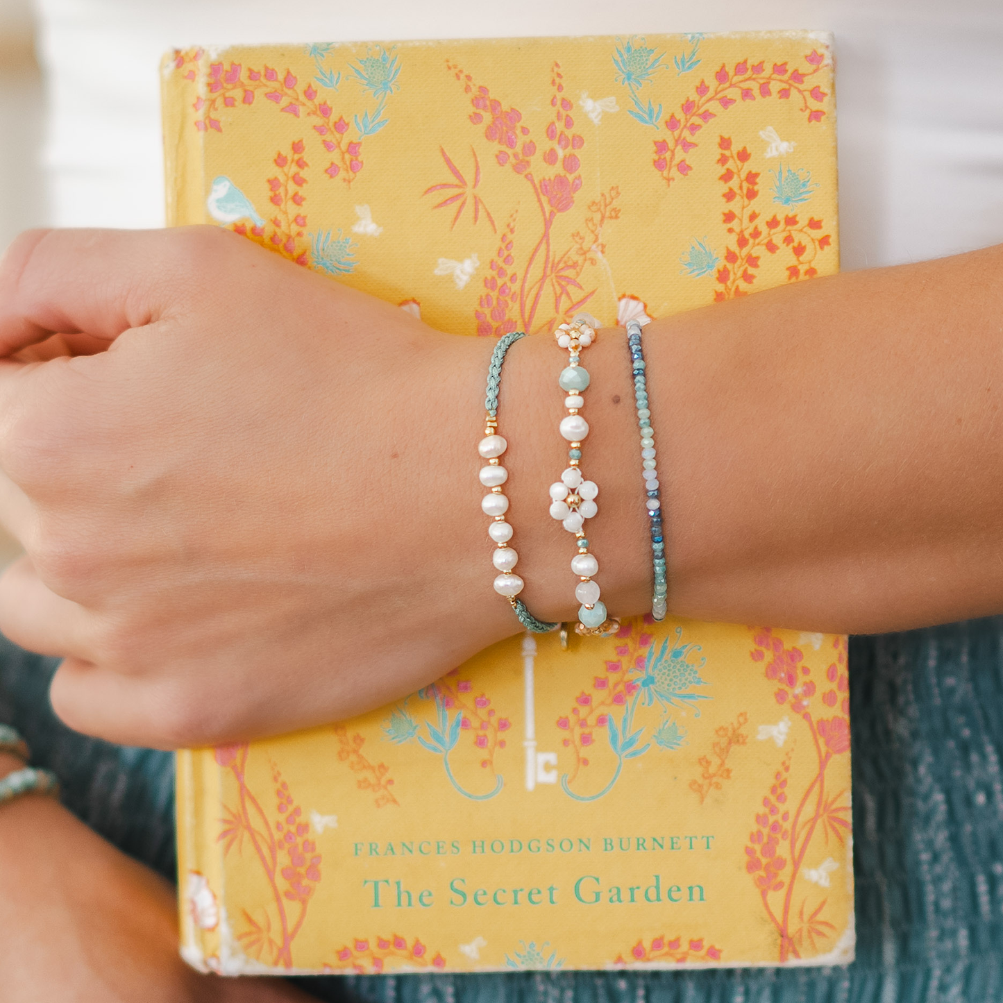 Person wearing multiple bracelets on a book titled 'The Secret Garden' by Frances Hodgson Burnett