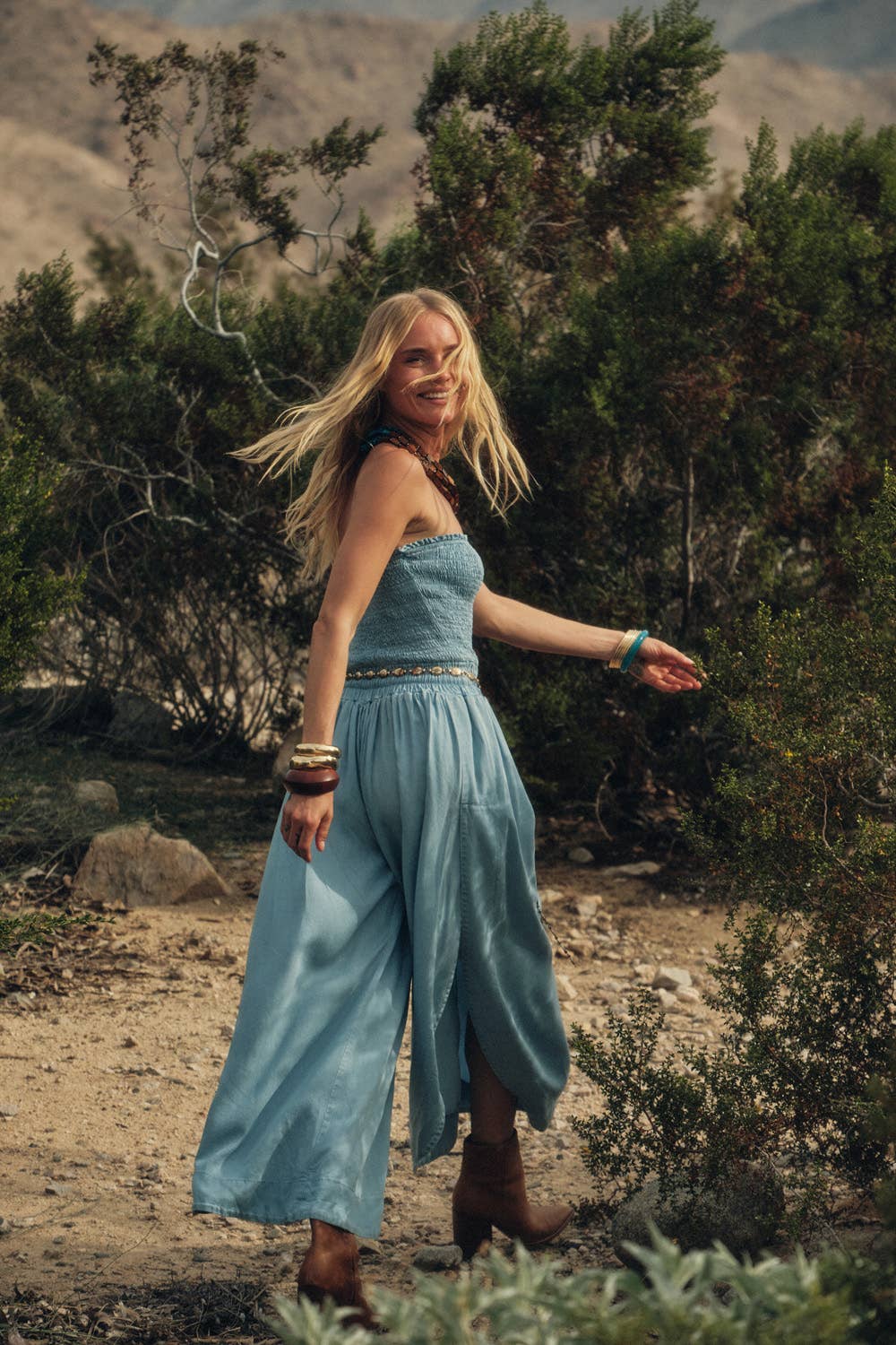 Woman in a blue dress standing in a desert landscape with greenery.