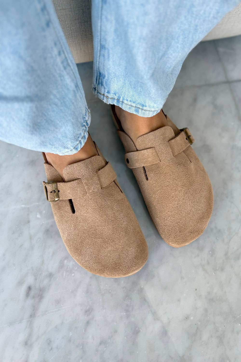 Latte suede clog featuring an adjustable side buckle and lightweight sole, styled with casual denim.