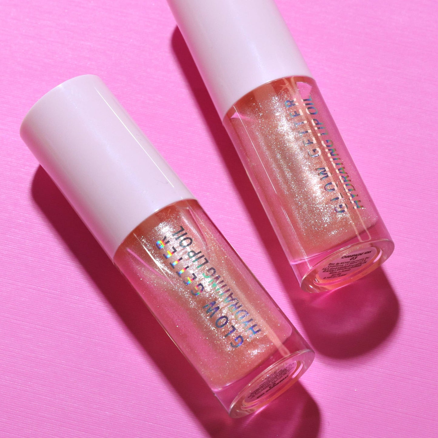Two lip glosses with glittery finish on a pink background