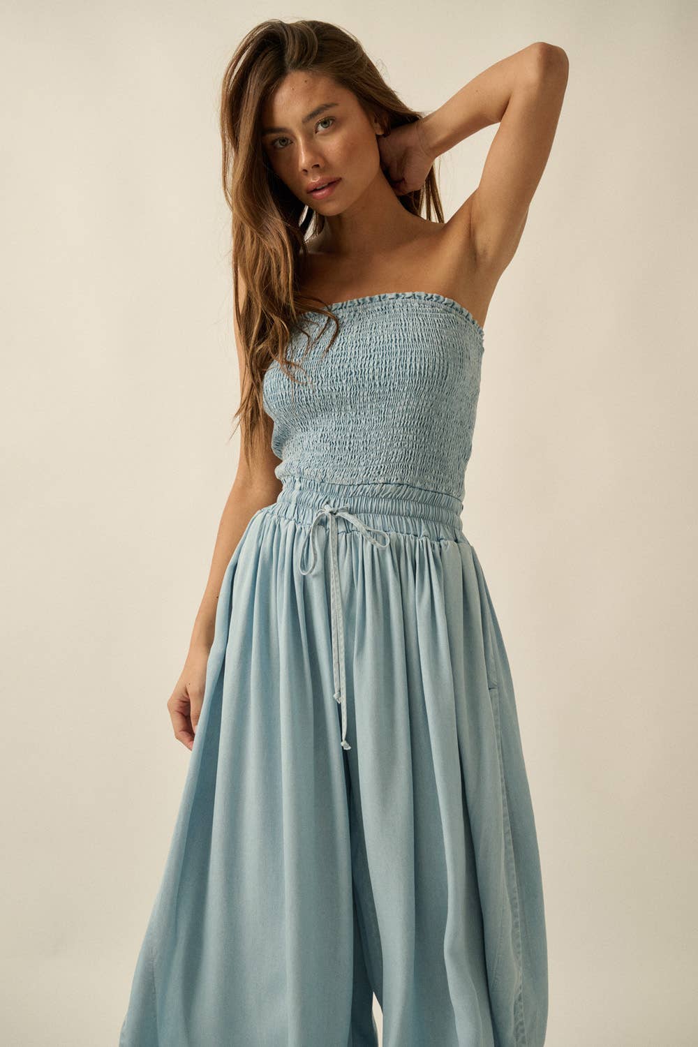 Woman wearing a light blue strapless jumpsuit against a plain background